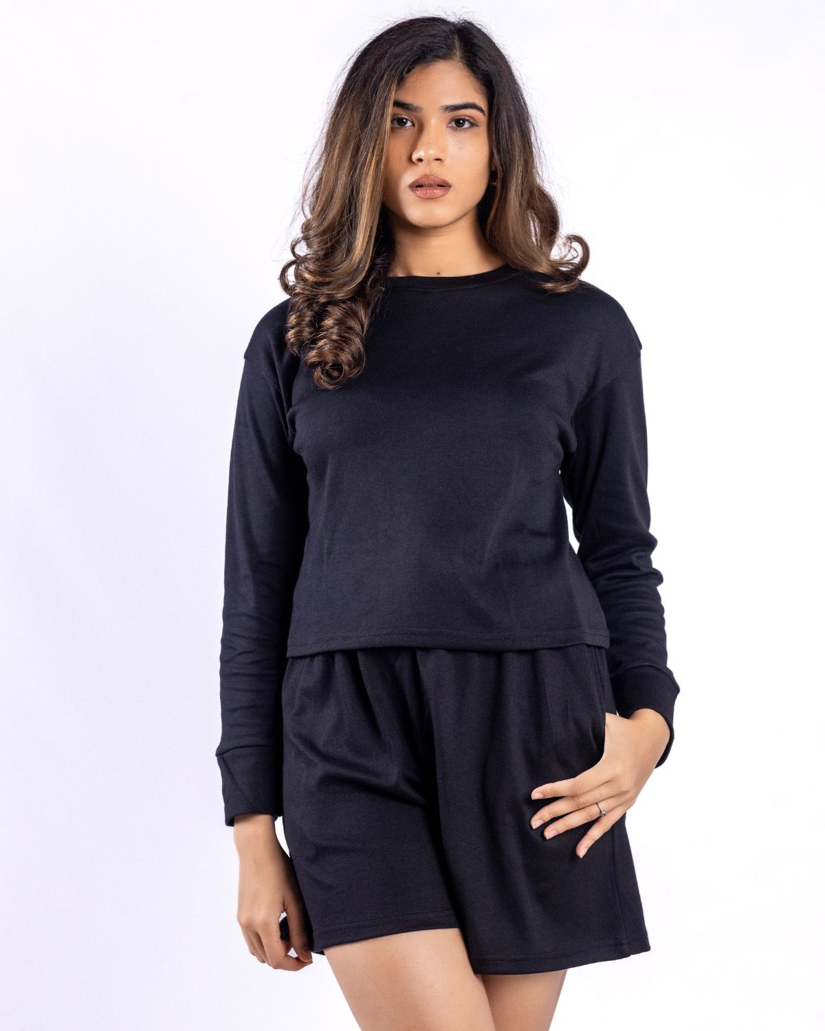 A woman wearing a stylish black long-sleeve top paired with matching black shorts.